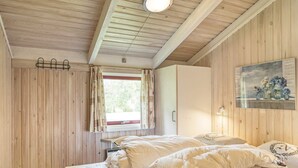 A bedroom with wooden walls, a bed with white bedding, a window with curtains, and a painting on the wall. - Cozy Cottage With Sauna - By Traum Ferienwohnungen (Vaeggerlose)