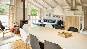A spacious living area with a large table, a sofa, and a dining area. There is a fireplace, a ceiling fan, and a view of the outdoors. - Cozy Cottage With Sauna - By Traum Ferienwohnungen (Vaeggerlose)