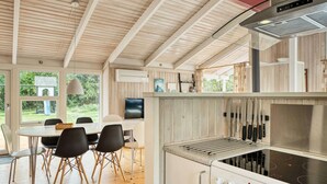 A modern kitchen with a built-in stove, a dining area with a table and chairs, and a view of the outdoors through large windows. - Cozy Cottage With Sauna - By Traum Ferienwohnungen (Vaeggerlose)