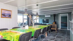 Ein Essbereich mit einem langen Tisch, der mit einer bunten Tischdecke bedeckt ist, schwarzen Stühlen, Pendelleuchten und einem Kamin.