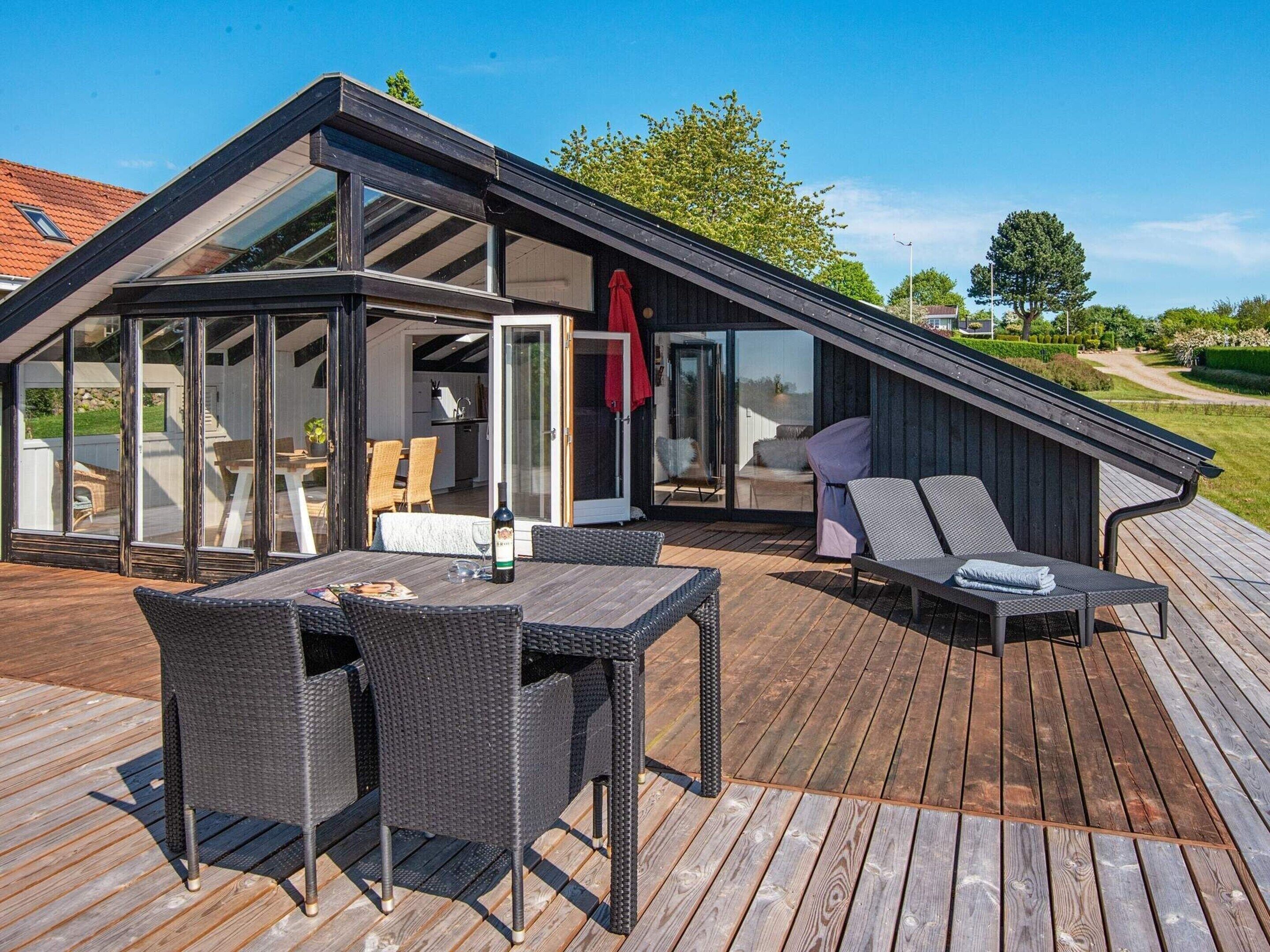 A modern house with a sloped roof, a covered patio with outdoor furniture, and a glass-enclosed dining area.