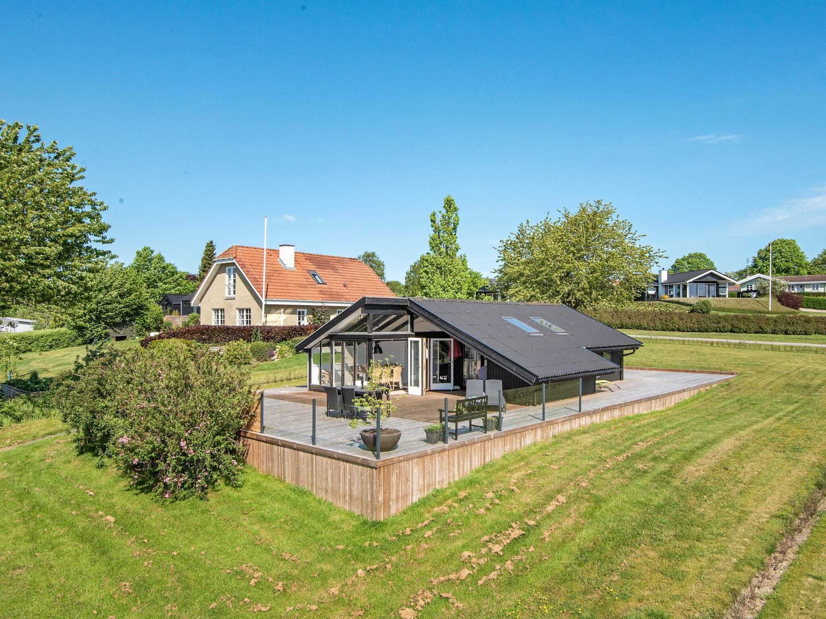 A modern house with a large deck, a conservatory, and a well-maintained lawn.