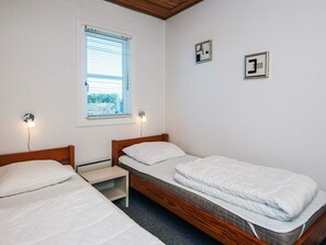 A room with two single beds, a window with blinds, and two wall-mounted light fixtures.