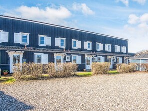 A row of dark blue townhouses with white-framed windows and doors, arranged in a linear fashion with a gravel driveway in front.