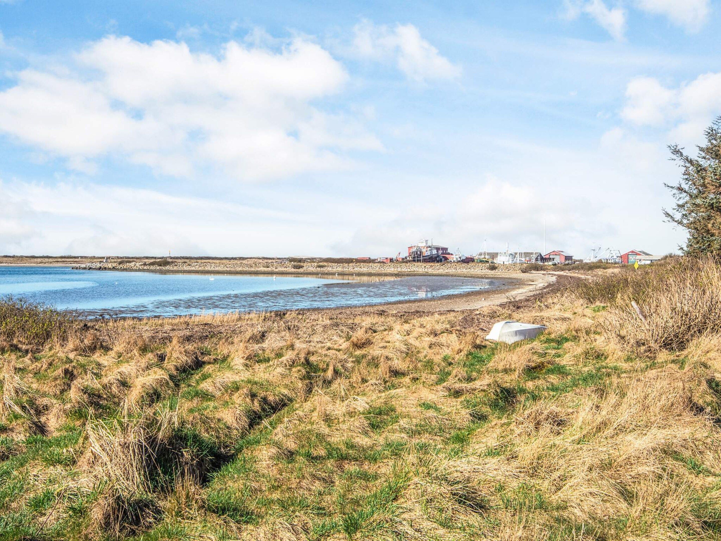 A coastal landscape with a clear sky, a sandy beach, and industrial buildings in the background.