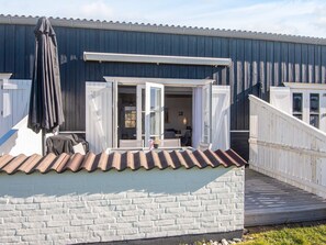 A wooden building with a white brick wall, a tiled roof, and a wooden deck leading to an open door. - 6 Person Holiday Home in Vestervig (Vestervig)
