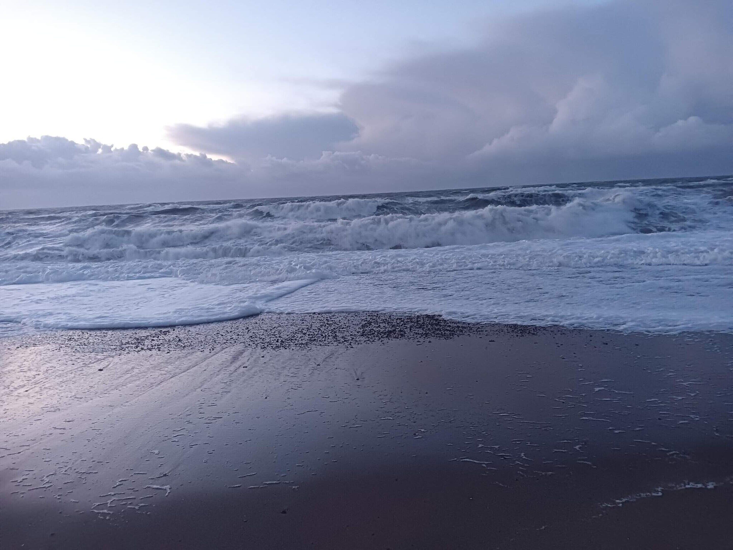 A beach with waves crashing onto the shore and a cloudy sky.