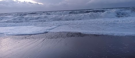 A beach with waves crashing onto the shore and a cloudy sky.