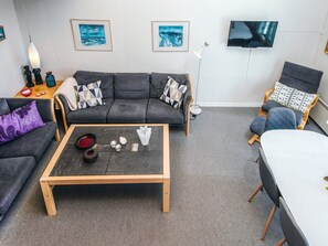 A modern living room with a grey sofa, a wooden coffee table, and a TV mounted on the wall.