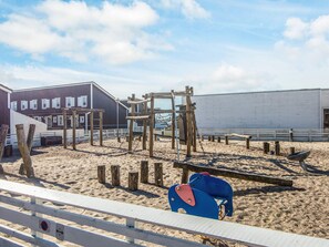 A playground with wooden structures and a sandy ground, surrounded by buildings.