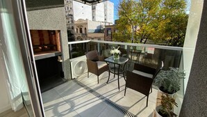 A balcony with a glass railing, a table, two chairs, and a potted plant.