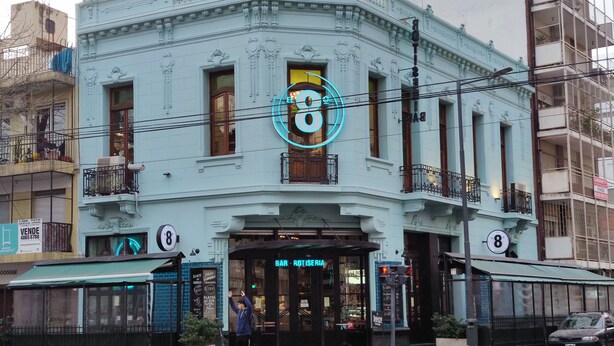 A light blue building with ornate architectural details, a neon sign, and a storefront labeled "BAR ROTESERIA".