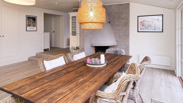 A dining area with a wooden table, wicker chairs, a hanging light fixture, and a fireplace. - 8 Person Holiday Home in Gilleleje (Gilleleje)