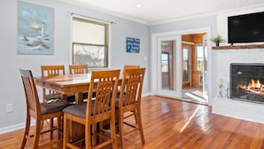A dining area with a wooden table and chairs, a fireplace, and a painting of a lighthouse. - Beautiful Bayfront with Sanctuary Private Beach  (Saxis)