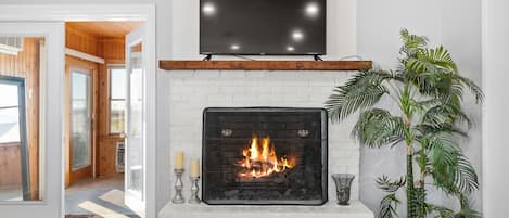 A fireplace with a TV above it, a potted plant, and a view into another room.
