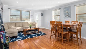 A living room with a beige sectional sofa, a coffee table, and a dining area with wooden chairs and a table. - Beautiful Bayfront with Sanctuary Private Beach  (Saxis)