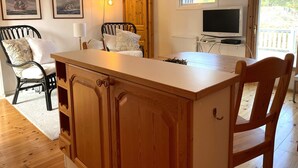 Une pièce chaleureuse avec une table à manger en bois, deux chaises, un petit meuble, un téléviseur fixé au mur et des tableaux marins encadrés.