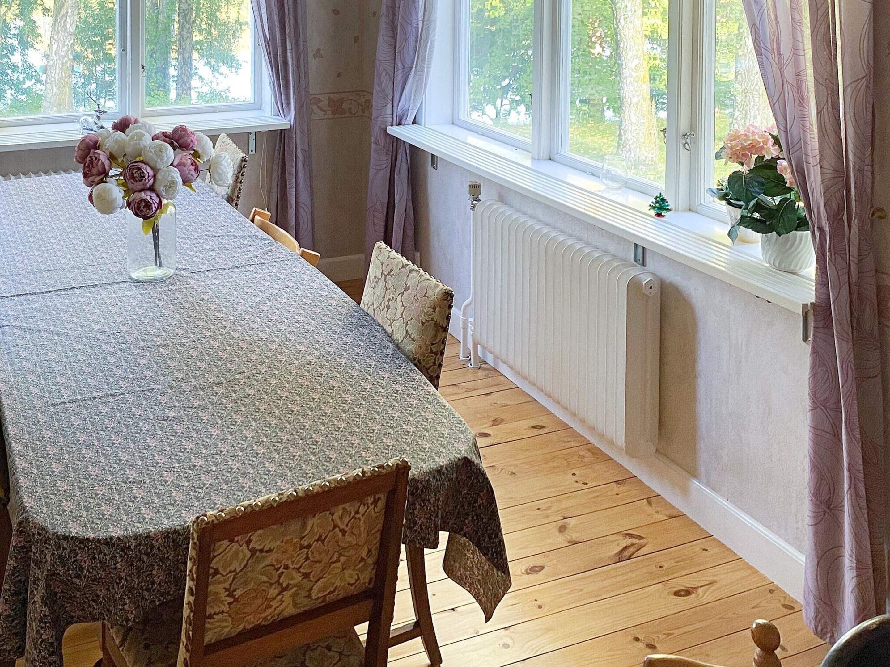 Un coin repas avec une table dressée pour quatre personnes, un radiateur et une fenêtre avec des rideaux.