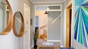 A hallway with a wooden floor, a blue bench, a potted plant, and a colorful abstract painting on the wall. - 13 Person Holiday Home in Billingfors (Billingsfors)