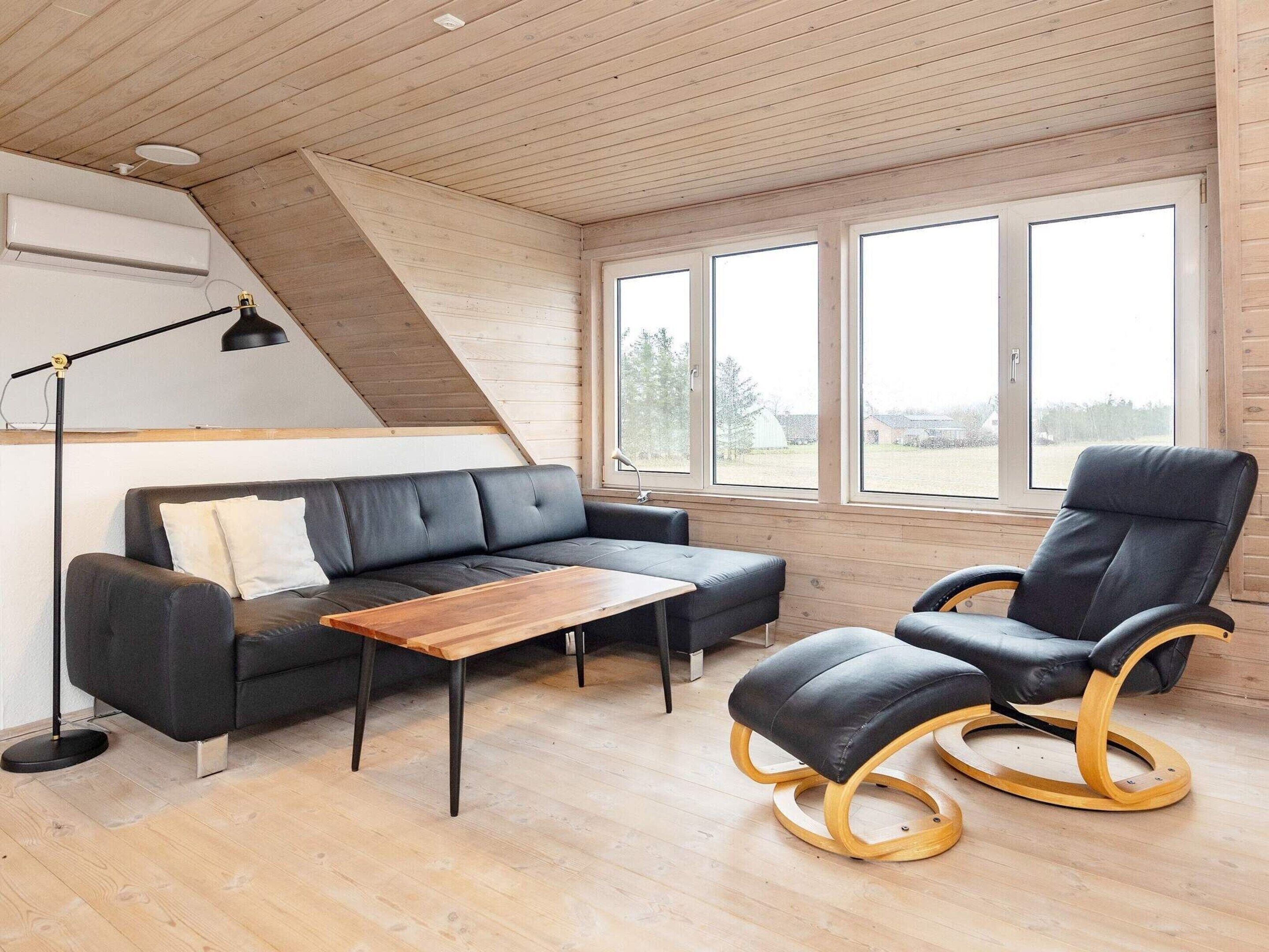 Een moderne woonkamer met een bank, een houten salontafel, een zwarte lederen fauteuil en een vloerlamp.
