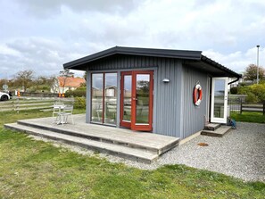 A small, modern building with a grey exterior and red-framed glass doors, featuring a wooden deck and outdoor seating. - 3 Person Holiday Home in Lottorp (Löttorp)