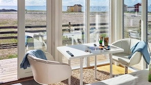 A conservatory with a table and chairs, overlooking a beach with a wooden fence and a small building. - 3 Person Holiday Home in Lottorp (Löttorp)