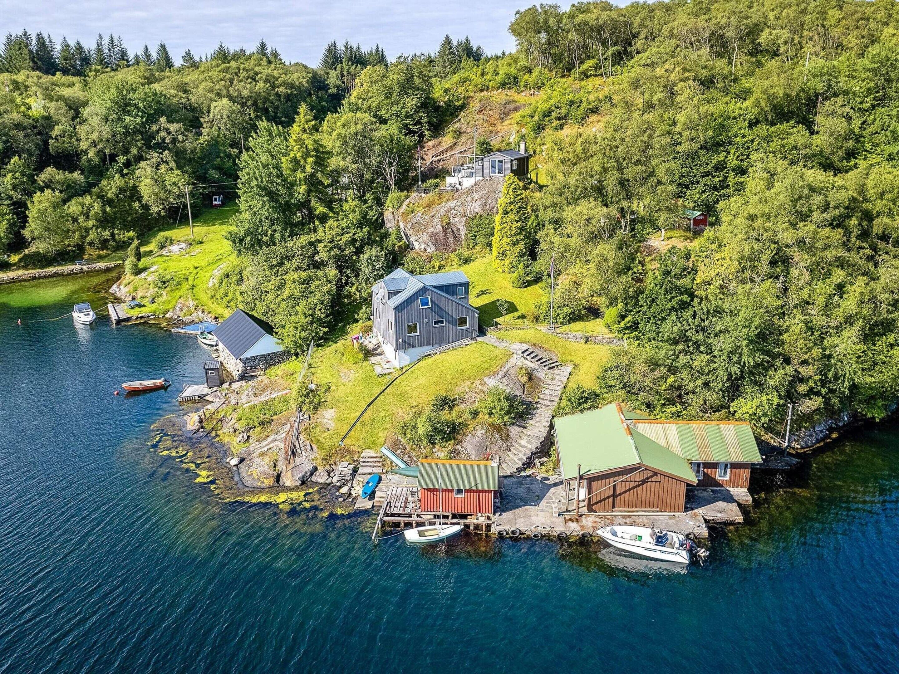 Una propiedad costera con una casa principal, una cabaña más pequeña y un muelle con barcos.
