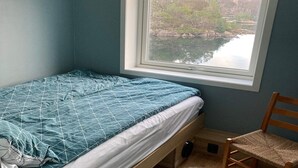 A small bedroom with a single bed, a window with a view of a lake and trees, and a wooden chair. - 8 Person Holiday Home in Sveio-by Traum (Sveio)