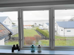 Une fenêtre donnant sur un espace verdoyant, un bâtiment blanc et une étendue d’eau.