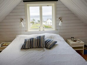 A bedroom with a large bed, two bedside lamps, a nightstand with a clock, and a window with a view of a house and trees. - 4 Star Holiday Home in Hoviksnas (Höviksnäs)