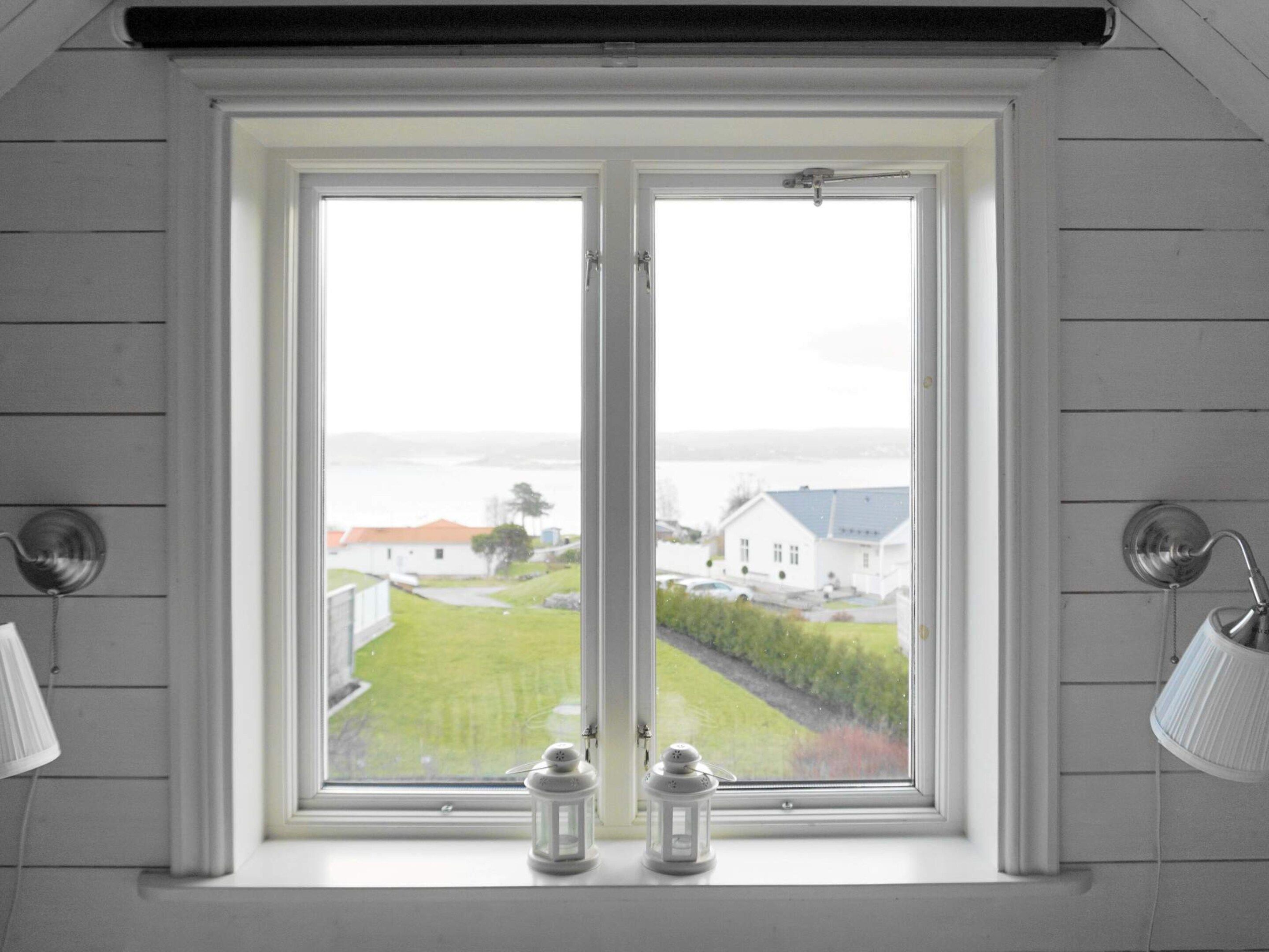 A room with a window overlooking a residential area, two wall-mounted lamps, and two white lanterns on the windowsill.