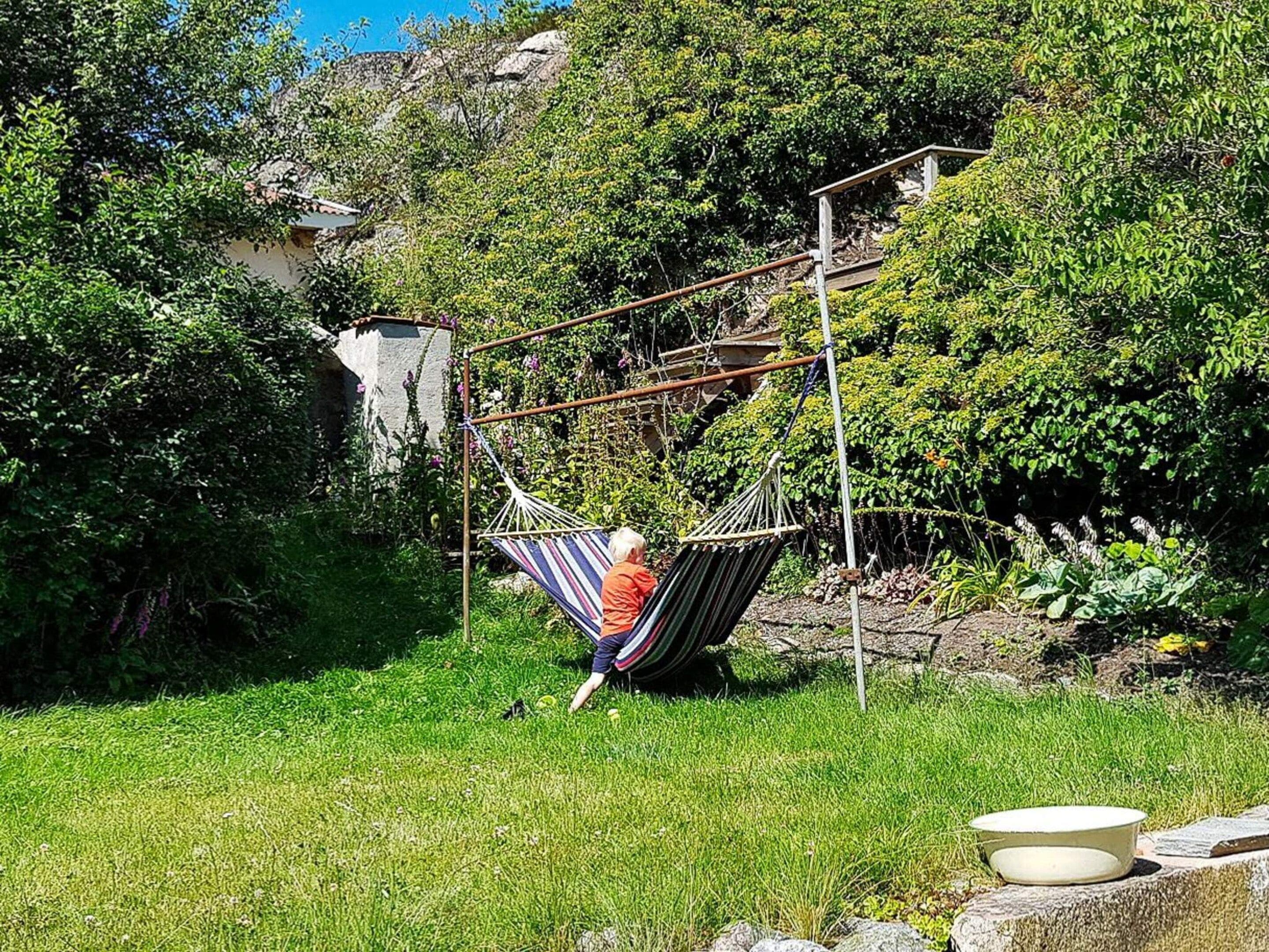 A hammock suspended between metal poles in a lush garden with a stone wall and greenery in the background.
