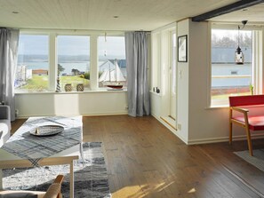 A spacious room with large windows, a wooden floor, a red bench, and a table with a placemat. - 4 Star Holiday Home in Hoviksnas (Höviksnäs)