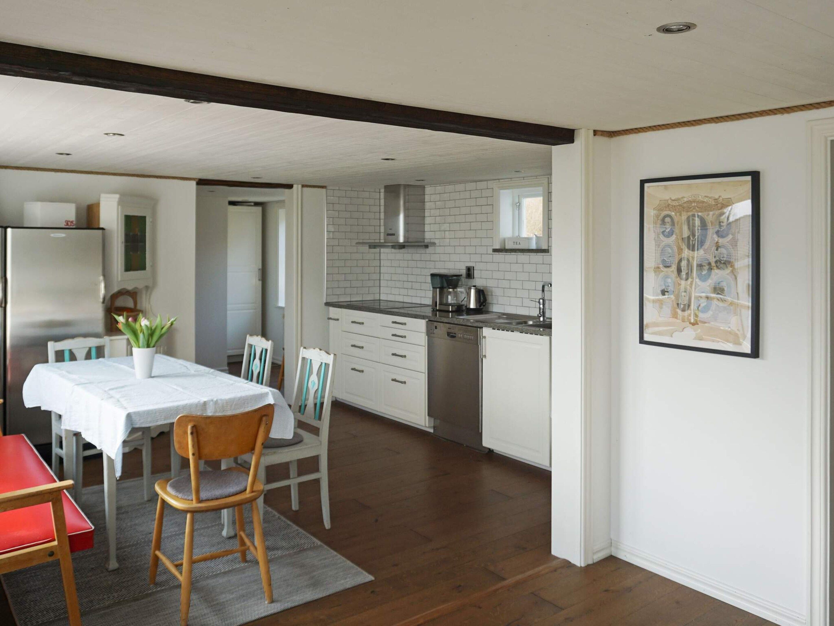 Een moderne keuken met witte kasten, een roestvrijstalen koelkast en een eethoek met een tafel en stoelen.