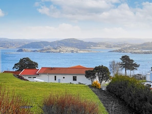 A coastal property with a white building featuring a red roof, situated on a grassy slope overlooking a large body of water and distant hills. - 4 Star Holiday Home in Hoviksnas (Höviksnäs)