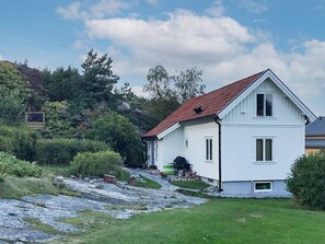 A white two-story house with a red roof, a small porch with outdoor furniture, and a stone pathway leading to the entrance.