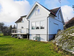 A two-story house with a balcony and a small deck, surrounded by a grassy yard and a rocky hillside. - 4 Star Holiday Home in Hoviksnas (Höviksnäs)