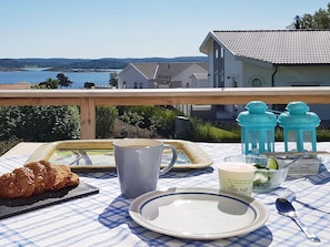 A table set with a croissant, a mug, a plate, a glass of milk, and a container of cream cheese on a balcony overlooking a lake and houses. - 4 Star Holiday Home in Hoviksnas (Höviksnäs)