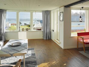 A spacious room with large windows, a wooden floor, a red bench, and a table with a placemat. - 4 Star Holiday Home in Hoviksnas (Höviksnäs)