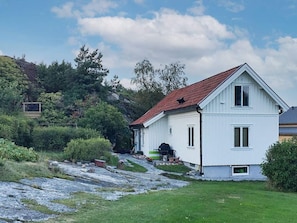 Une maison blanche à deux étages, avec un toit rouge, un petit porche et un chemin de pierre menant à l’entrée.