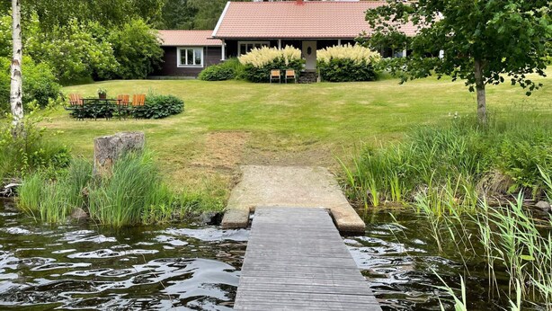 A house with a red roof, surrounded by a well-maintained lawn and a wooden dock over a pond. - 8 Person Holiday Home in Skyllberg-by Traum (Skyllberg)