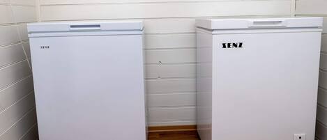 Deux réfrigérateurs blancs, portant la marque « SENZ », sont placés dans un coin d’une pièce dont le sol est en bois et les murs sont blancs.