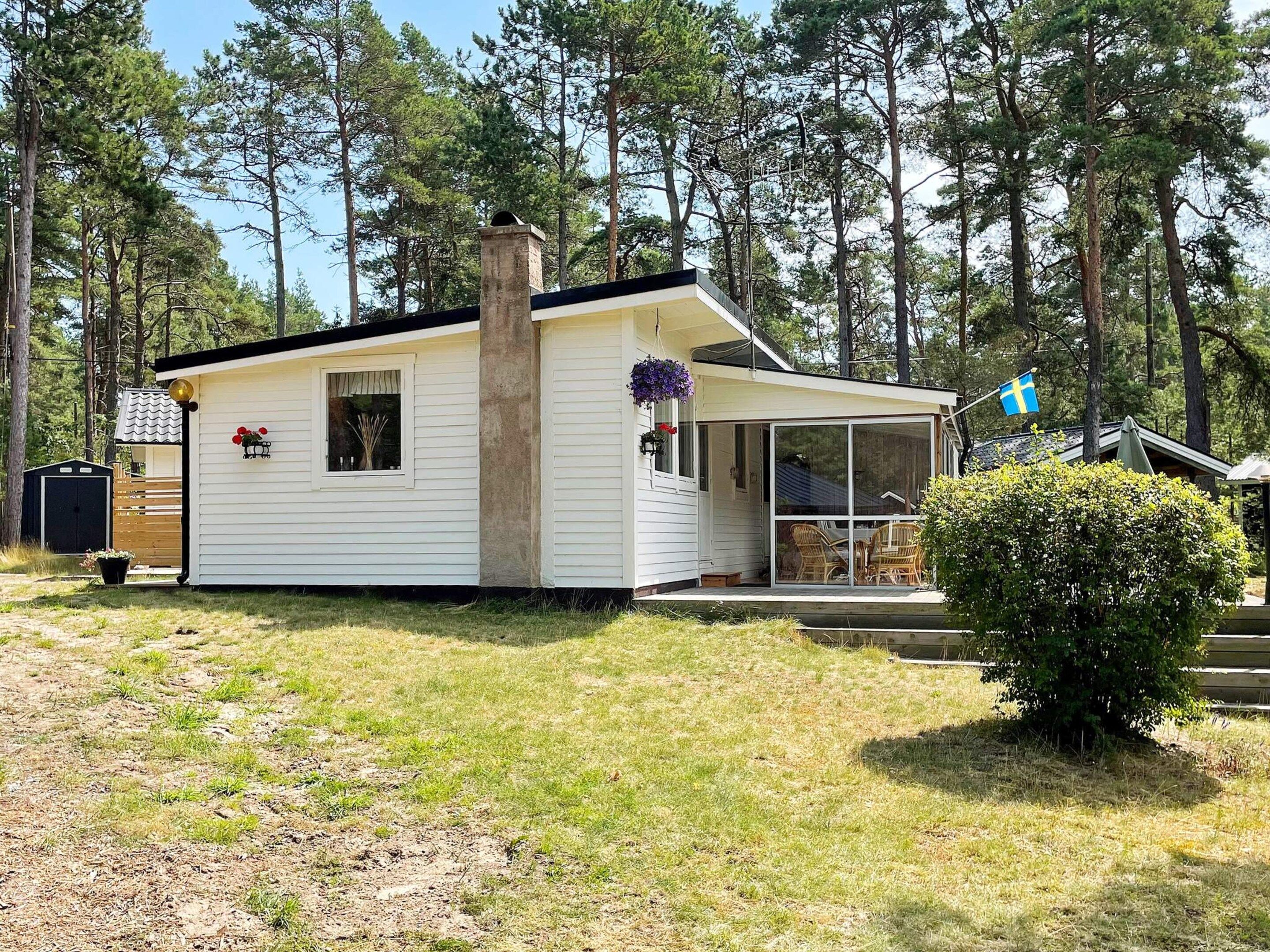 A single-story cabin with a covered porch, a chimney, and a Swedish flag.
