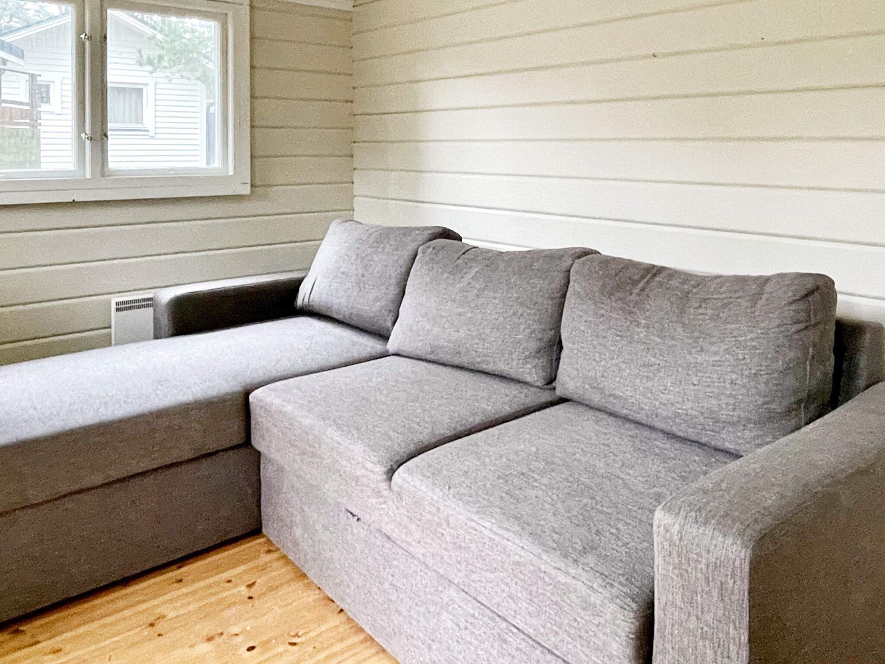 A grey sectional sofa in a room with wooden flooring and white paneled walls.