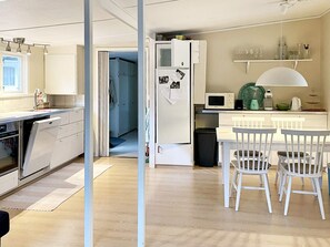 Une cuisine moderne avec des meubles blancs, un four à micro-ondes, un évier et un coin repas avec des chaises blanches.
