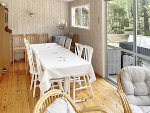 A dining area with a white table set for four, wooden chairs, a candelabra, and a view of the outdoors through a large window. - 4 Star Holiday Home in Yngsjo, Sverige (Yngsjo)