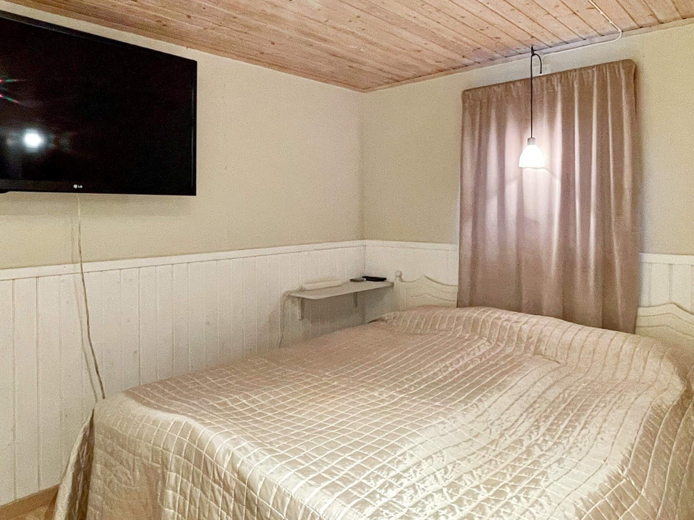Una habitación con cama, televisor montado en la pared, una mesita de noche y una cortina.