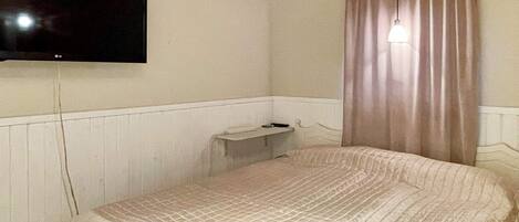 A room with a bed, a television mounted on the wall, a small bedside table, and a curtain.