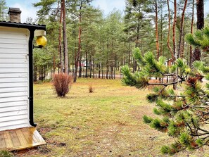 Una cabaña con terraza de madera, rodeada por un bosque de altos pinos.