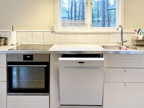 Una cucina con forno a incasso, lavastoviglie e una finestra vista alberi.